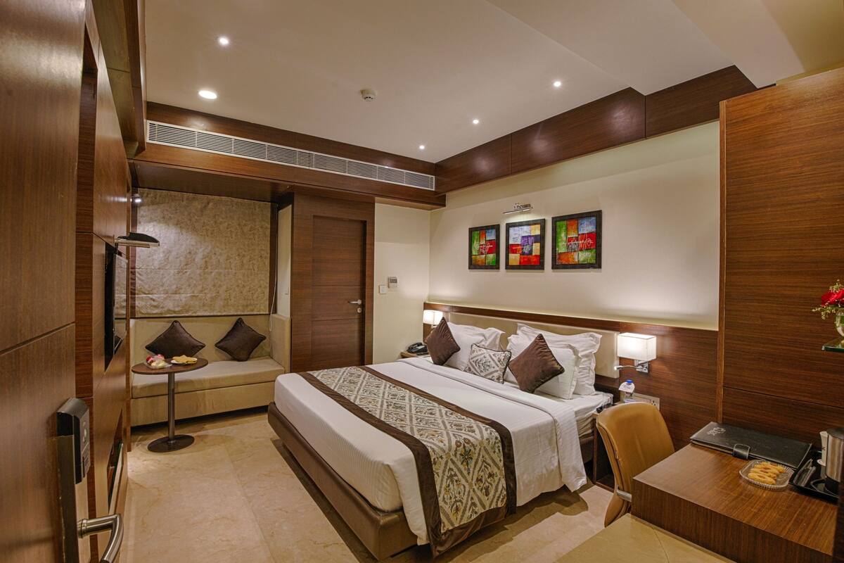 Habitación de hotel con una cama grande, un escritorio, una silla, una mesita y una obra de arte en la pared.