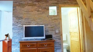 Ein Zimmer mit Steinwand, Holzschrank, Fernseher und einer Treppe.