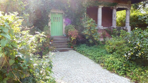A brick house with a green door, a cobblestone pathway leading to the entrance, and lush greenery surrounding the property. - Cy Twombly -. Villa-Hufeland in Berlin, quiet, 25 minutes by S-Bahn to the center (Berlin)