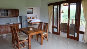 Amplia habitación con una mesa de comedor de madera, sillas, una cama y un balcón con vistas a zonas verdes.