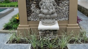 Una estatua de una deidad en un jardín, con un edificio de techo de tejas al fondo.