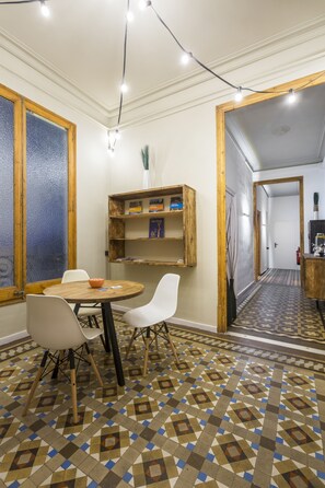A dining area with a round table, white chairs, a patterned floor, wooden shelves, and a mirror. - Casa Maca Guest House Boutique - Adults Only (Barcelona)