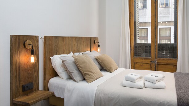 A neatly made bed with white linens and beige pillows, a wooden headboard, and a bedside table with a lamp. - Casa Maca Guest House Boutique - Adults Only (Barcelona)