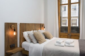 A neatly made bed with white linens and beige pillows, a wooden headboard, and a bedside table with a lamp. - Casa Maca Guest House Boutique - Adults Only (Barcelona)
