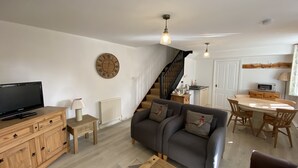 Un salon avec un canapé, un téléviseur, un meuble en bois, une lampe et une horloge au mur.