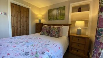 A bedroom with a bed, wooden wardrobe, two bedside tables with lamps, floral-patterned bedding, and a wall-mounted painting.