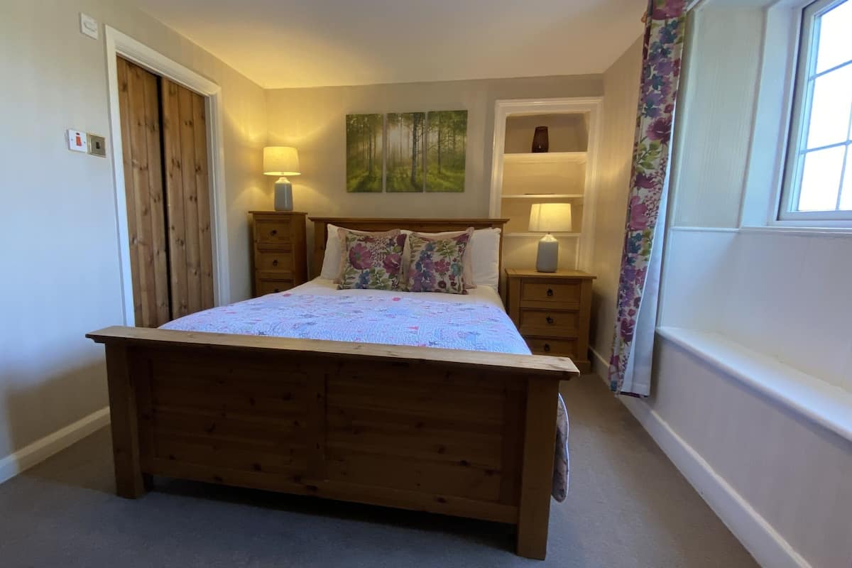 A bedroom with a wooden bed, two bedside tables with lamps, a floral curtain, and a painting on the wall.