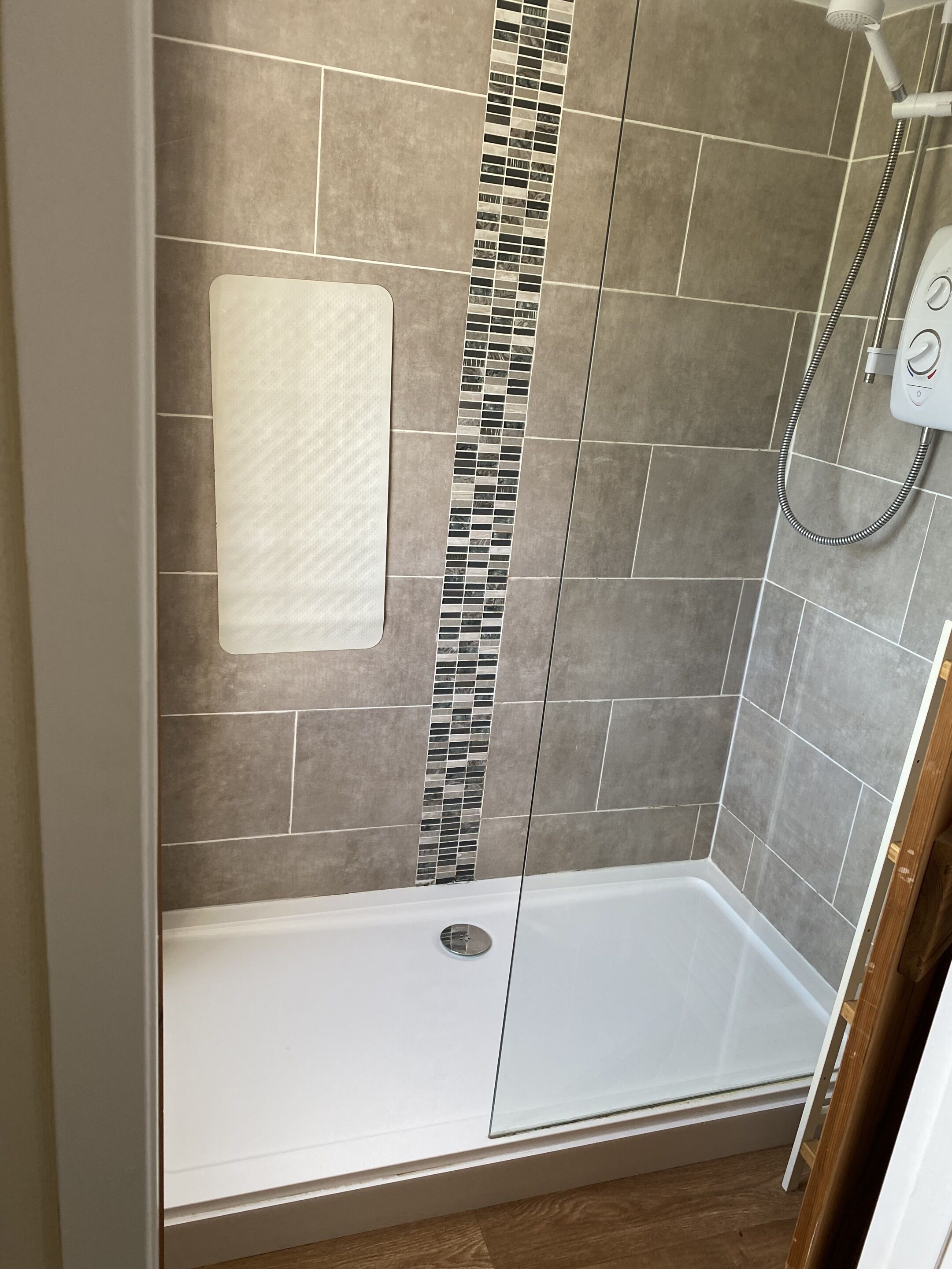 Zona de ducha con pared de azulejos, ducha blanca y desagüe.