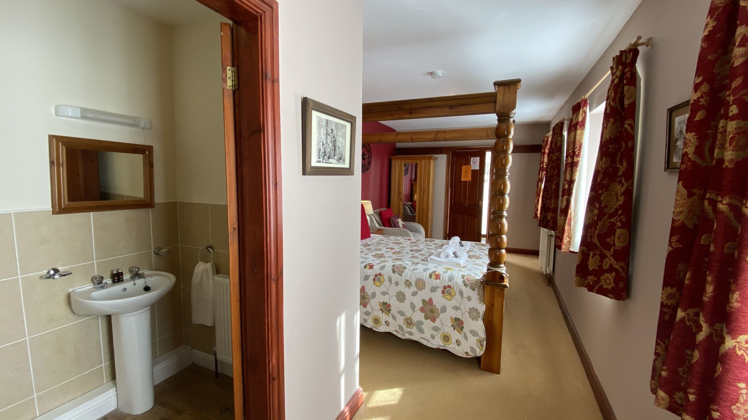 A bedroom with a four-poster bed, a wooden wardrobe, and a bathroom with a sink and mirror.