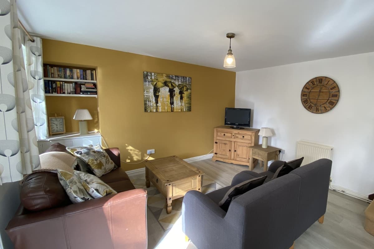 A living room with a sofa, armchair, coffee table, TV stand, and a painting on the wall.