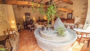 A rustic interior with a stone fountain, wooden furniture, and a hanging plant. - Hotel Nord (Estellencs)