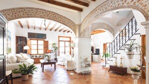 A spacious living area with a high ceiling, exposed wooden beams, and a staircase with decorative railings. - Hotel Nord (Estellencs)
