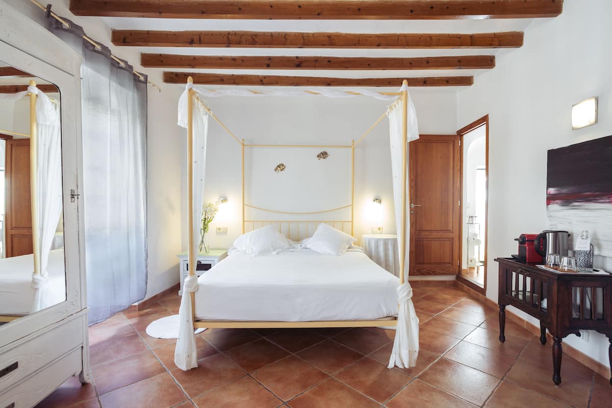 Uma cama de dossel com roupa de cama branca, vigas de madeira no teto e piso de azulejos.