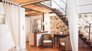 A cozy room with a bed, a wicker chair, a small table with a lamp, a stone wall, and a staircase. - Hotel Nord (Estellencs)