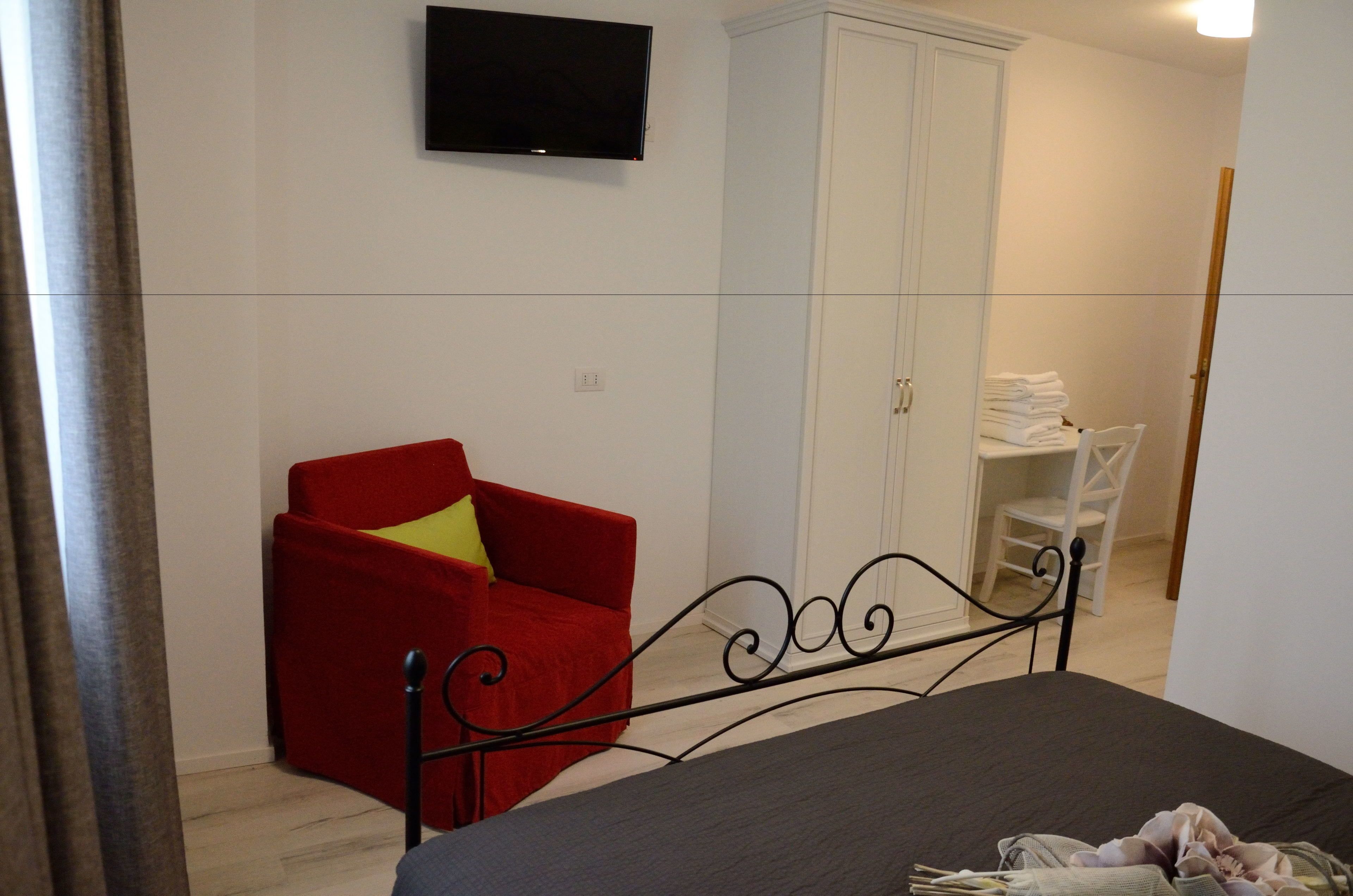 A bedroom with a bed, a red armchair, a television on the wall, and a white wardrobe.