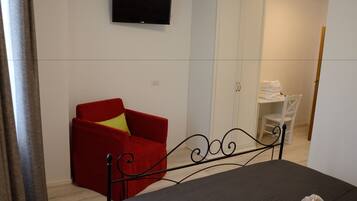 A bedroom with a bed, a red armchair, a television on the wall, and a white wardrobe.