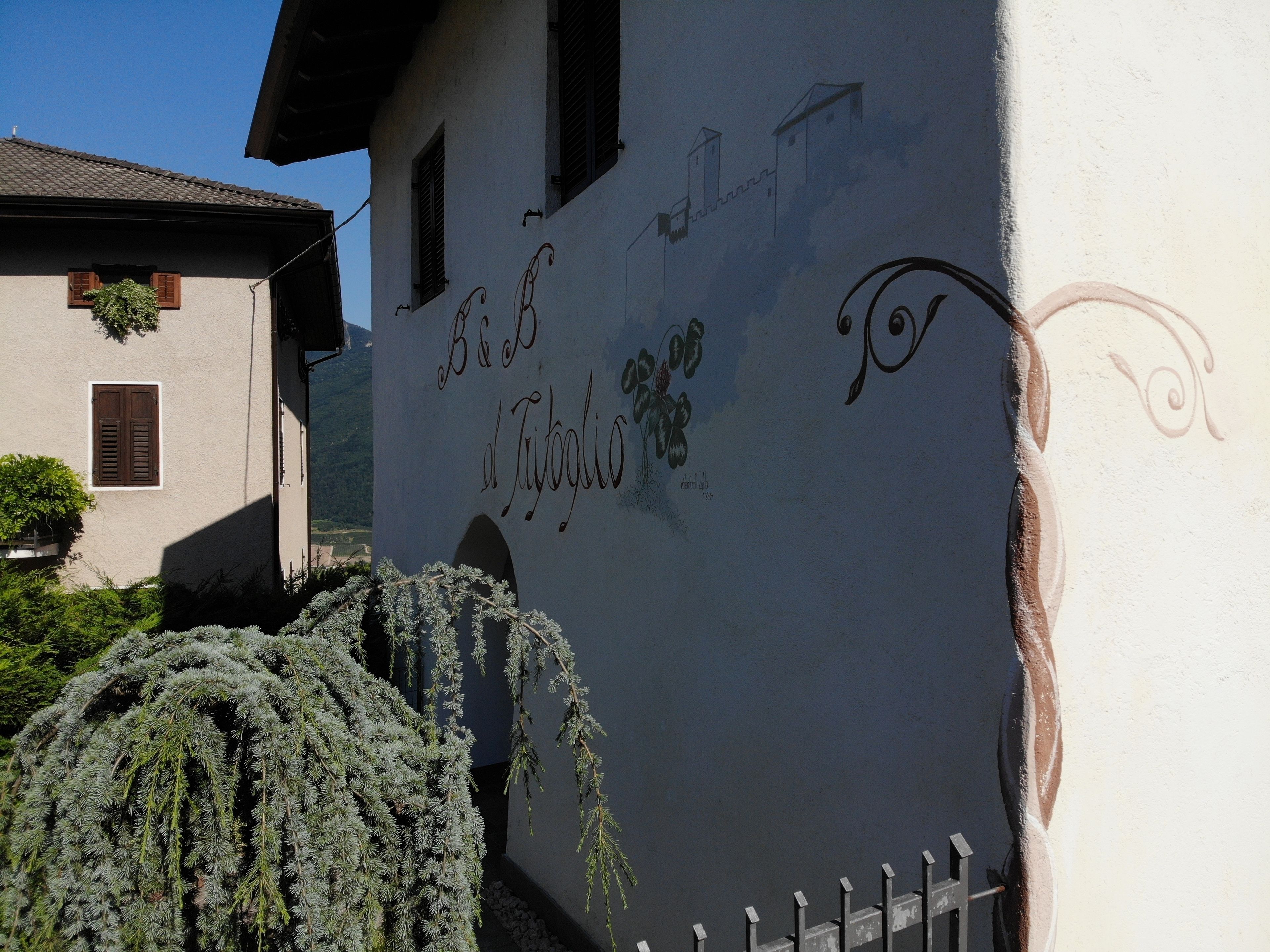 Un edificio con facciata bianca, un cartello con la scritta 'B&B del Tiscalio' e un recinto bianco di fronte.