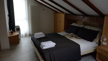 Un dormitorio con cama, mesitas de noche, un radiador y una ventana con cortinas.