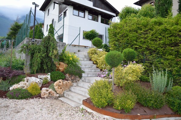 A white house with a stone staircase leading to the entrance, surrounded by various plants and shrubs. - B&B al Trifoglio (Campodenno)