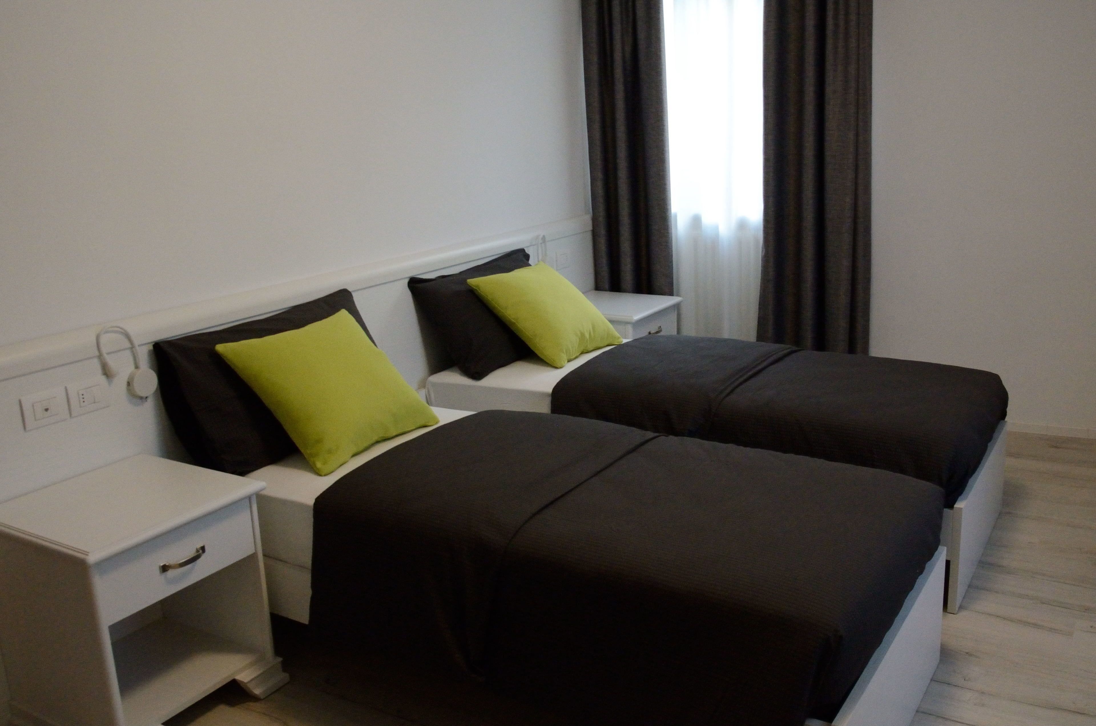 Quarto de hotel com duas camas de solteiro, cada uma com travesseiro e mesa de cabeceira.