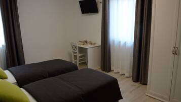 A bedroom with two beds, a desk, a TV, and a wardrobe.