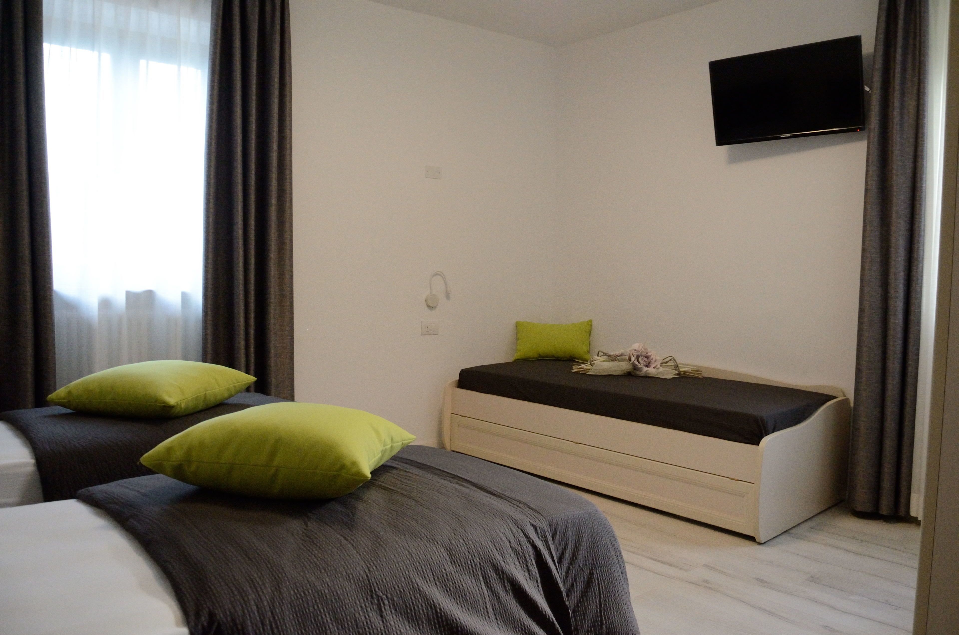Ein Hotelzimmer mit zwei Betten, einem Flachbildfernseher, einem Nachttisch und einem Fenster mit Vorhängen.