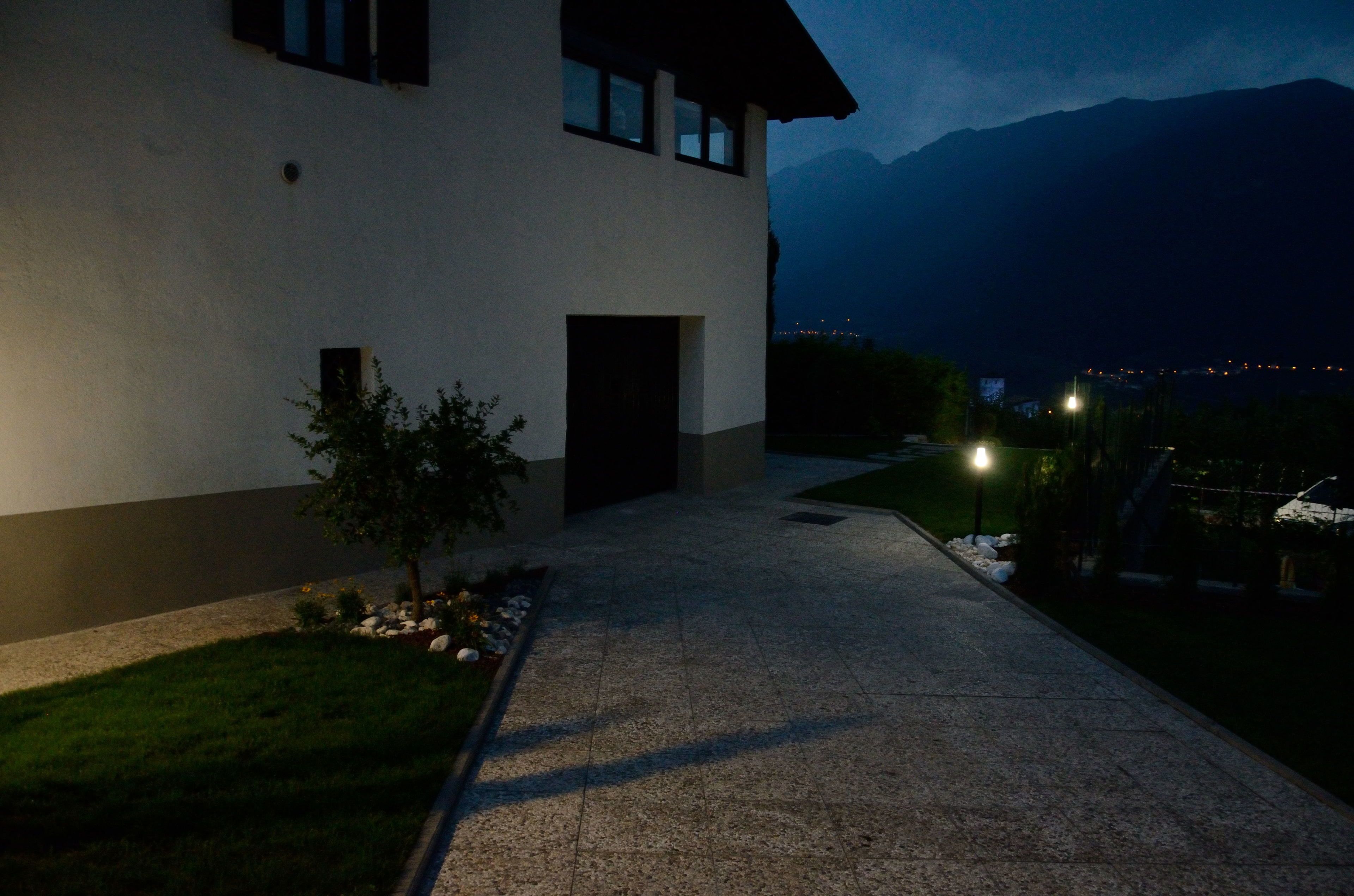 A modern two-story house with a paved driveway leading to the entrance, surrounded by a well-maintained lawn and a mountain backdrop.