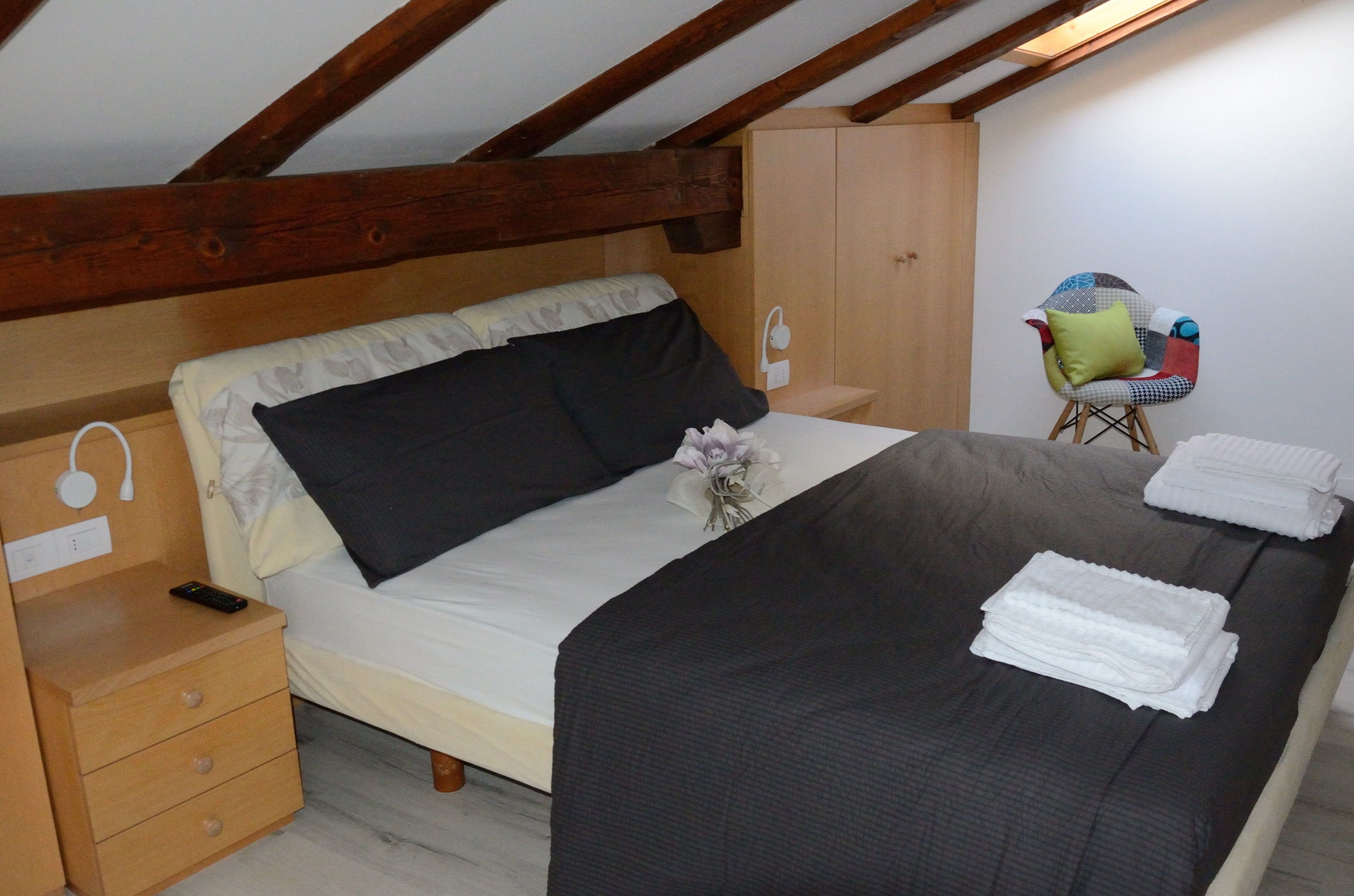 A bedroom with a bed, a nightstand, a wooden wardrobe, a chair, and a small table.