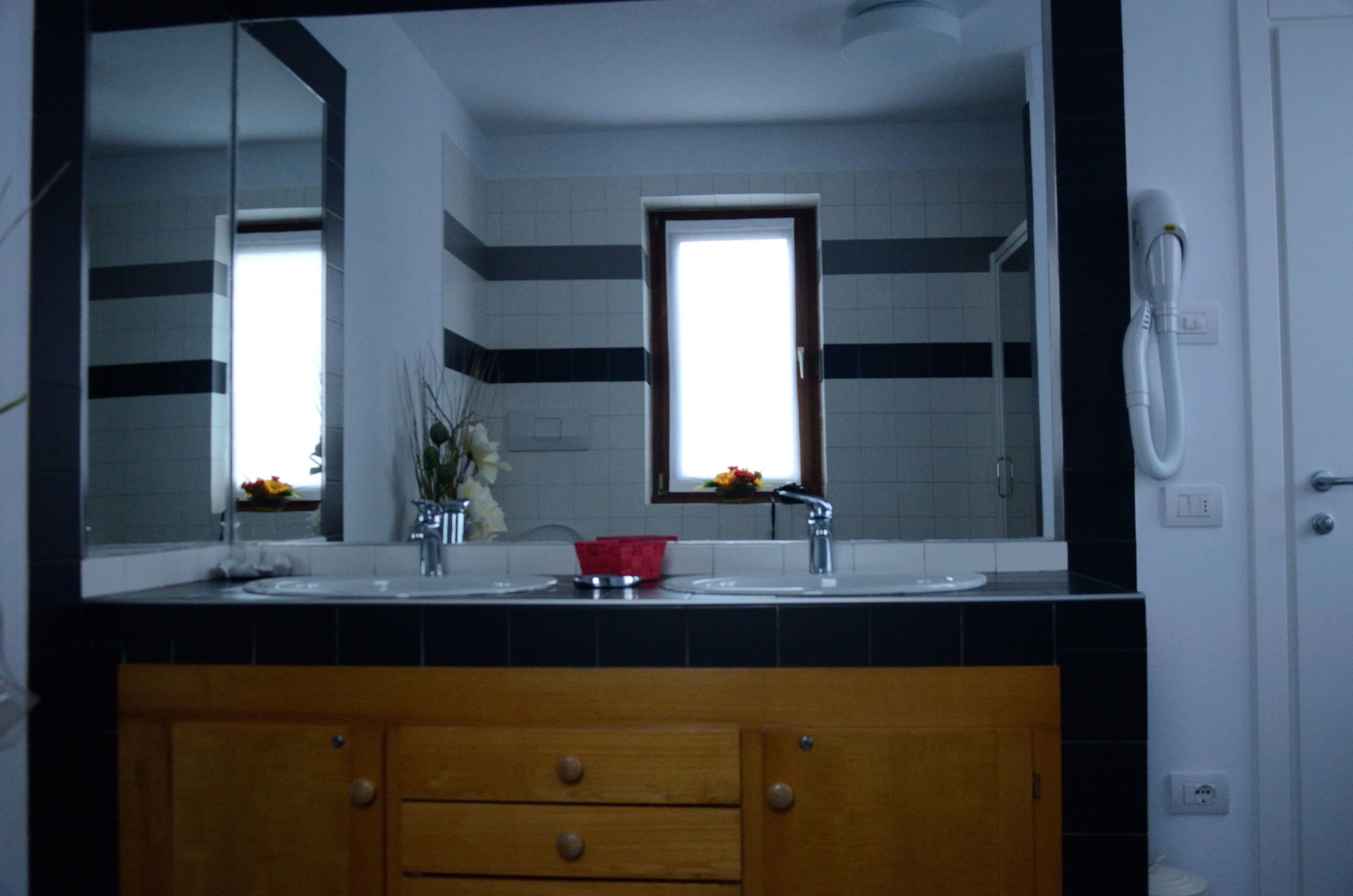 Un baño con un espejo grande, dos lavamanos, un mueble de madera con cajones y una ventana con vistas a flores afuera.