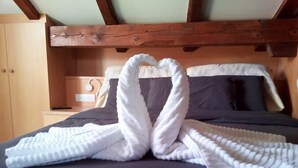 Una cama con un edredón oscuro y una toalla dispuesta en forma de corazón.