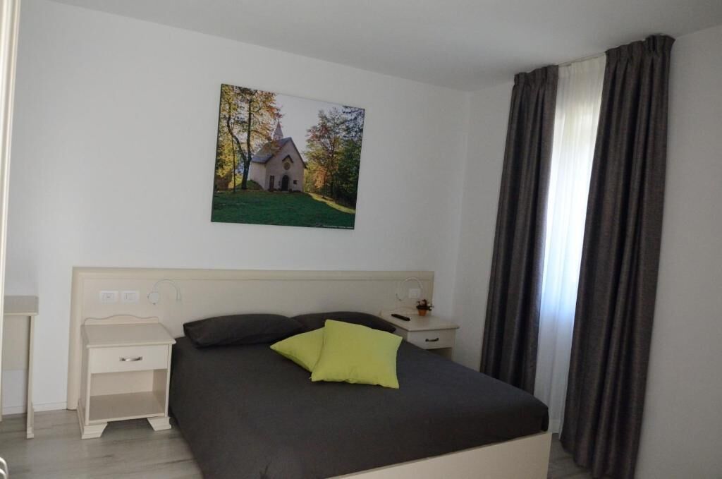 Una camera da letto con un letto, un comodino, una lampada e un quadro raffigurante una chiesa appeso al muro.