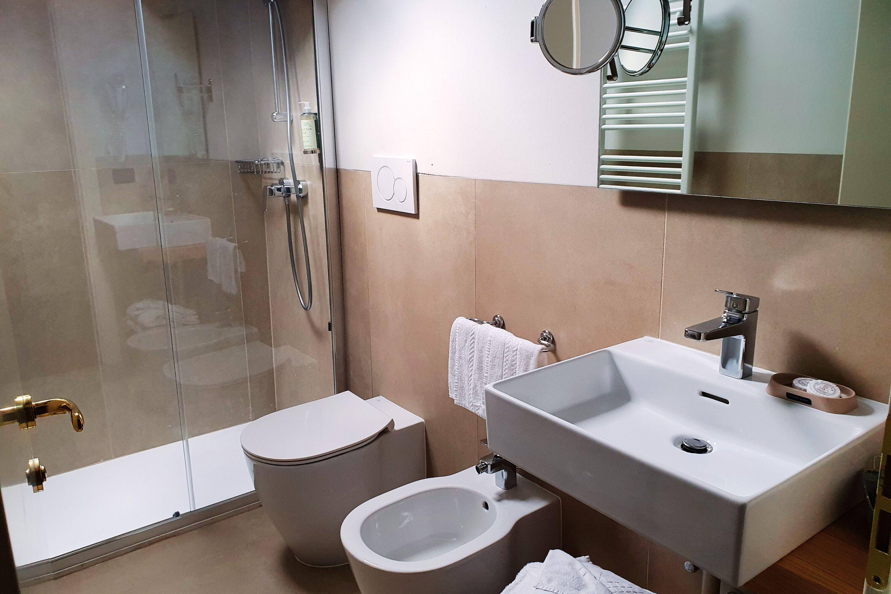 A modern bathroom with a glass-enclosed shower, a toilet, a bidet, and a sink with a mirror above it.