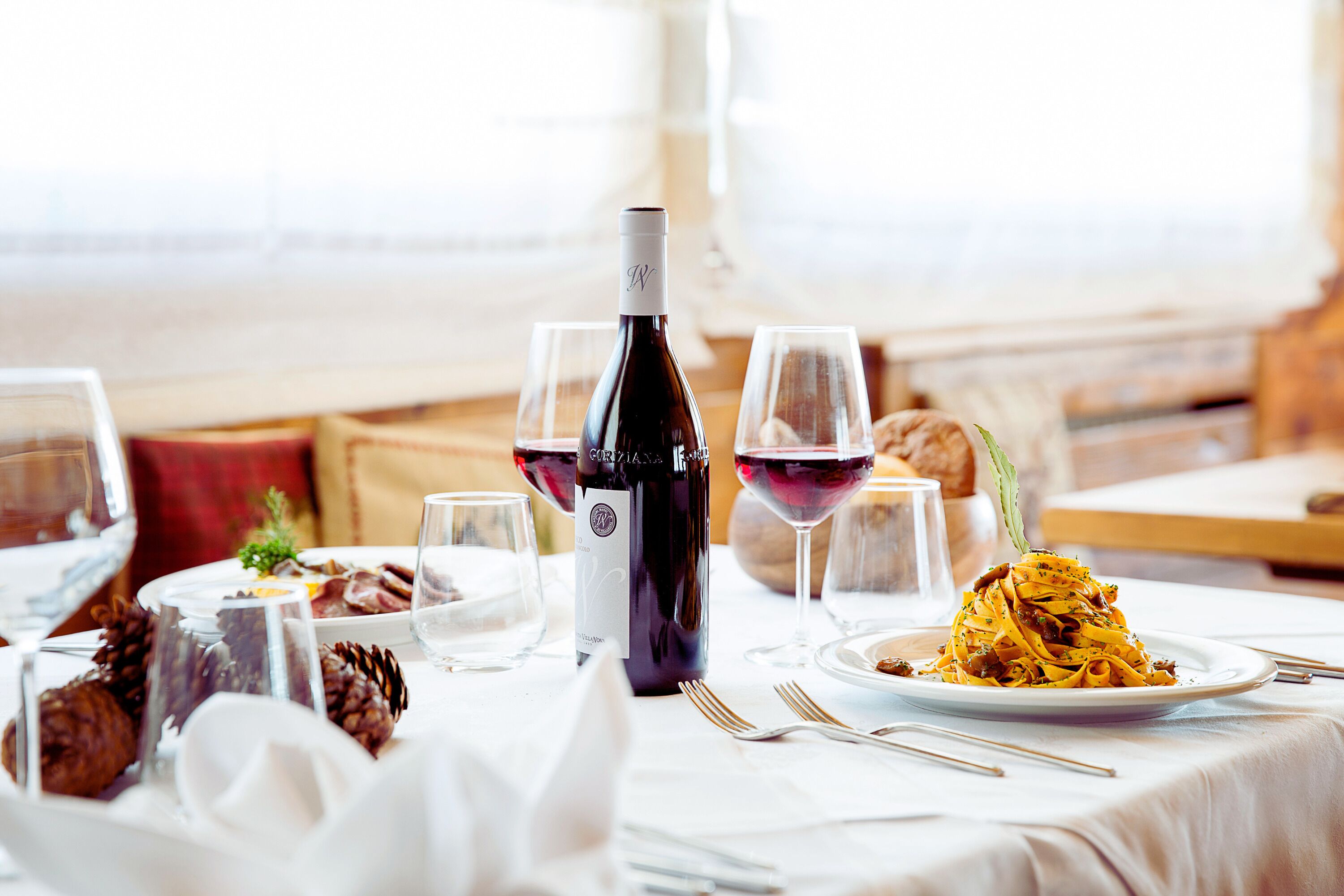 Une table à manger dressée avec une bouteille de vin, des verres et une assiette de pâtes.