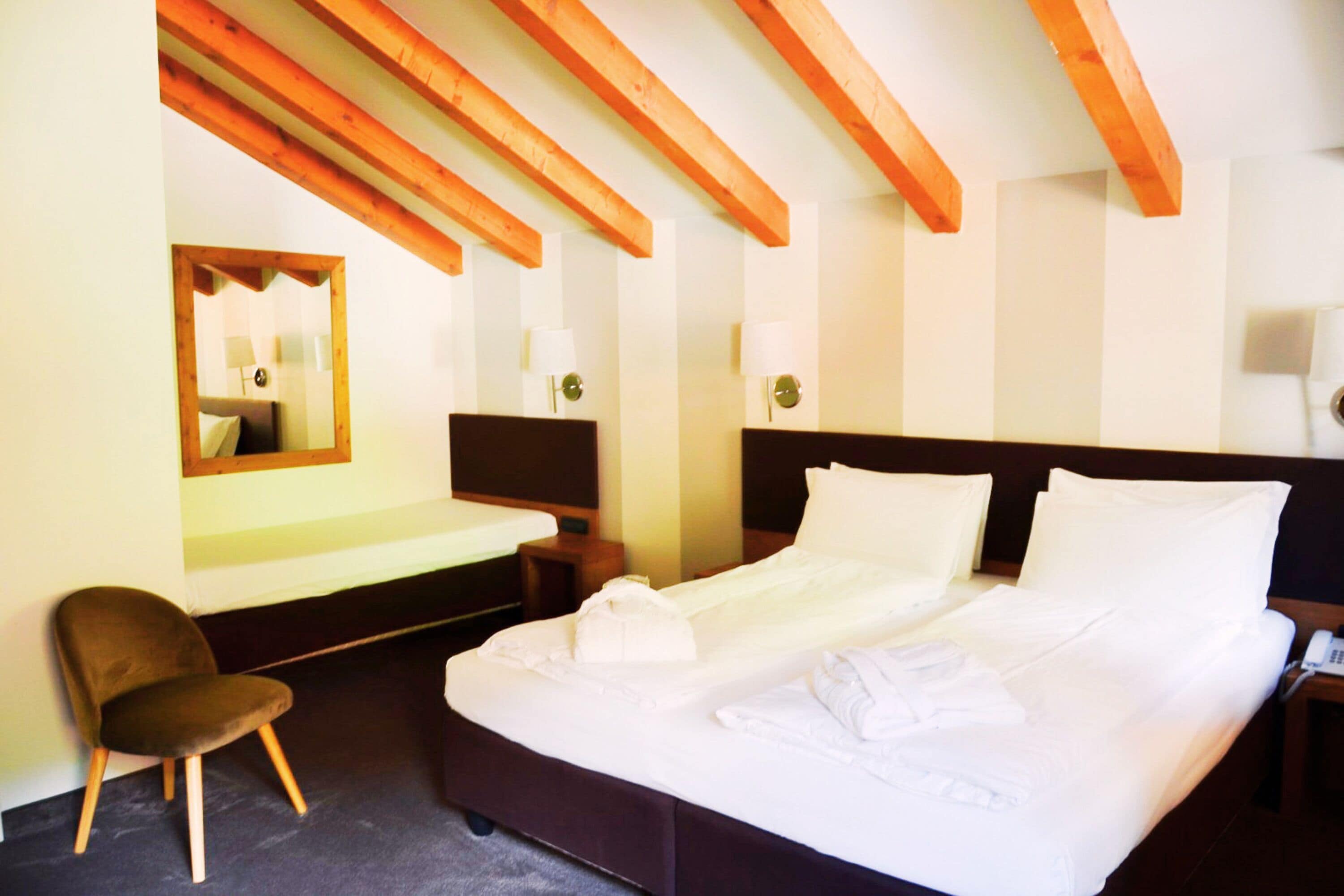 Une chambre d’hôtel avec un grand lit, des poutres en bois au plafond, une chaise, un bureau avec une lampe et un miroir au mur.