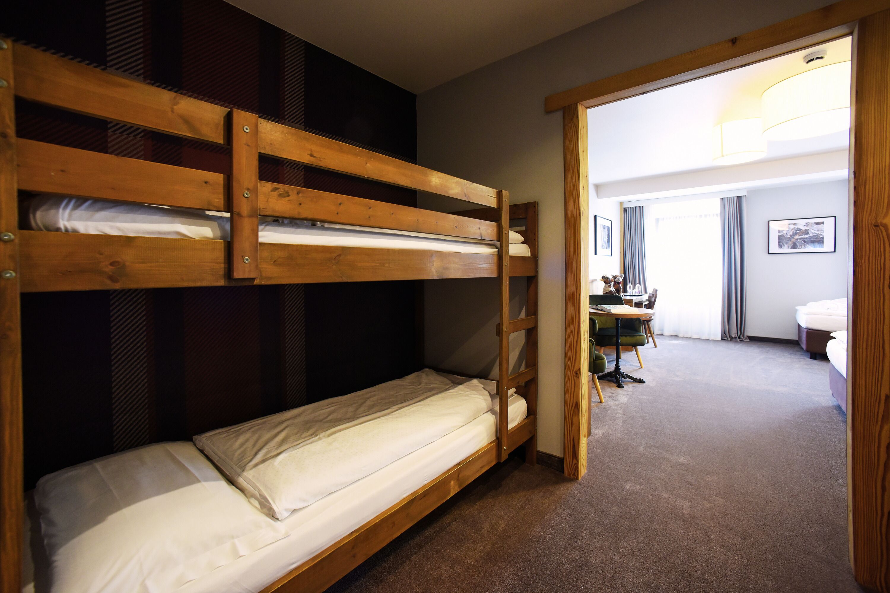 A bunk bed room with a desk and chair, a bathroom with a toilet and sink, and a door leading to another room.