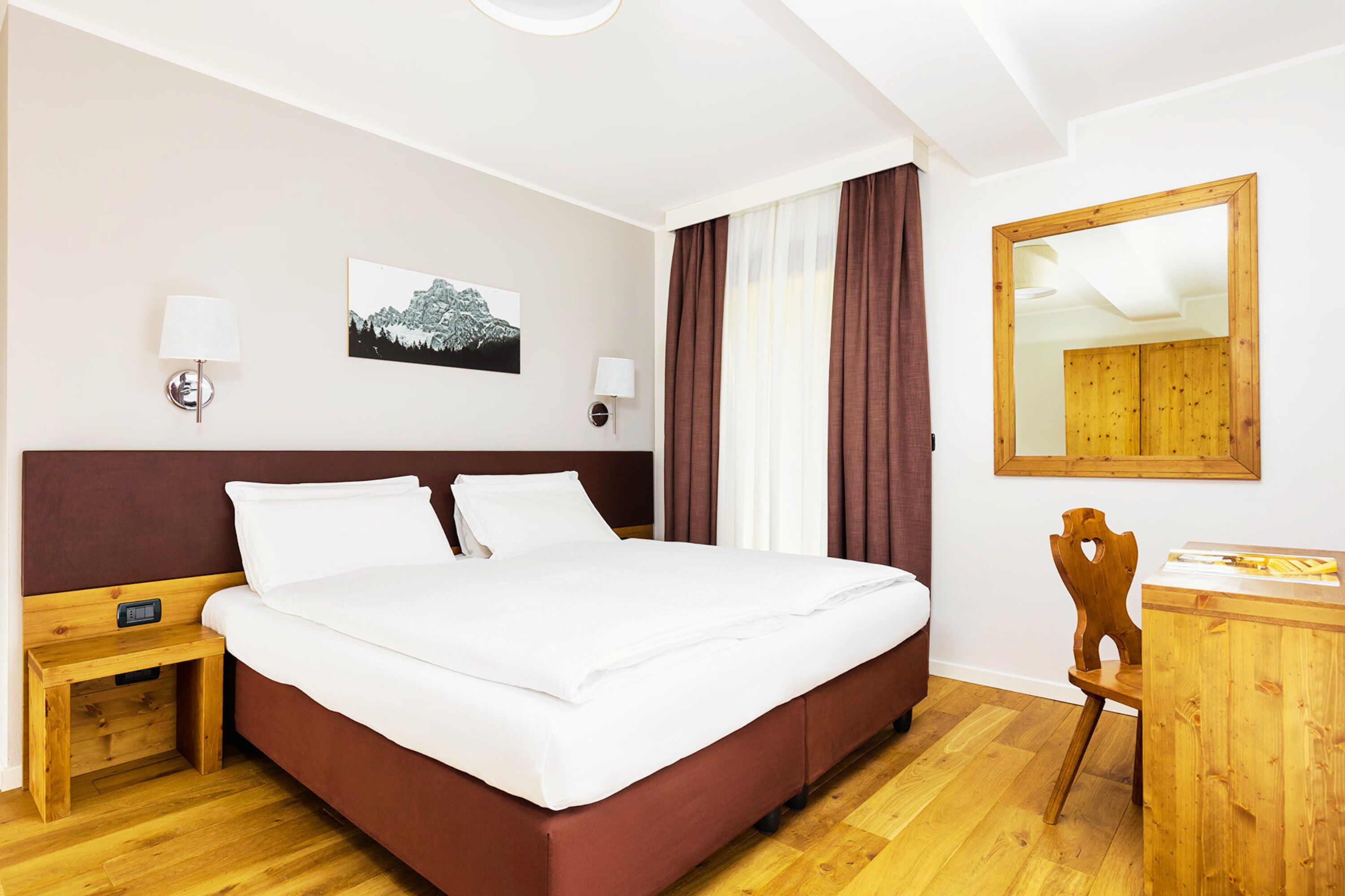 Una habitación de hotel con cama, mesita de noche, lámpara, silla, escritorio y espejo.