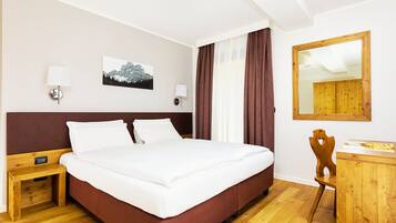 Una habitación de hotel con cama, mesita de noche, lámpara, silla, escritorio y espejo.