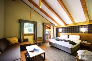 A hotel room with a bed, a sofa, a table, and a chair. There are wooden beams on the ceiling and a window with curtains. - Hotel Orso Grigio (Selva di Cadore)