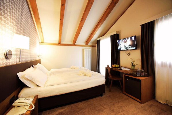 Une chambre d’hôtel équipée d’un lit, d’un téléphone sur la table de chevet, d’un bureau avec un ordinateur et d’un téléviseur fixé au mur.