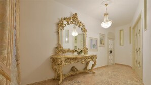 A room with a marble floor, a gold ornate console table, a large mirror, and a chandelier.
