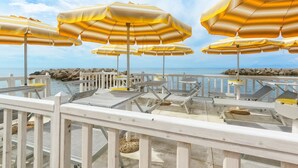A deck with multiple yellow umbrellas, white railings, and lounge chairs overlooking a body of water.