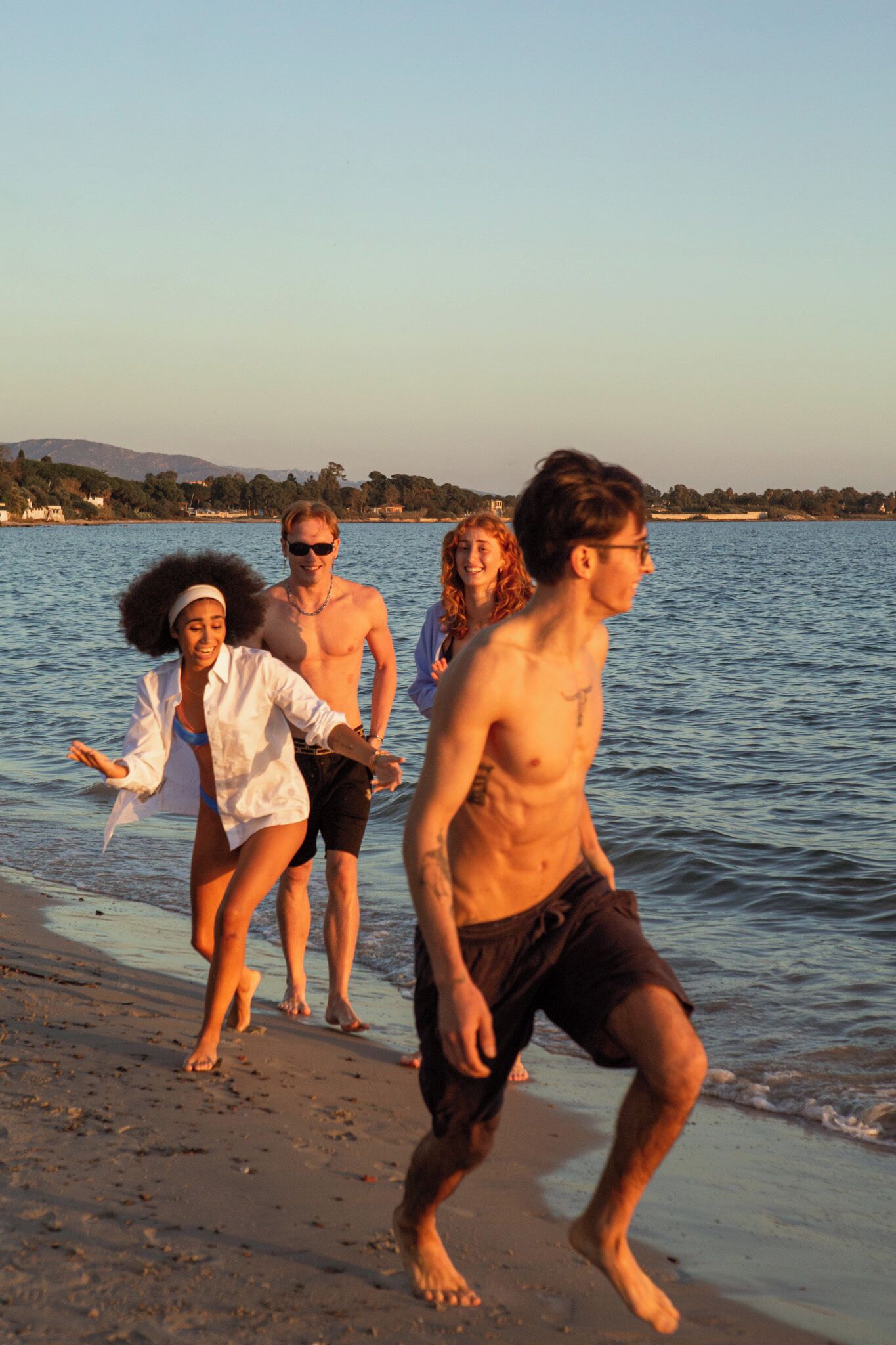 A group of people walking along a beach with a body of water and a distant shoreline in the background.