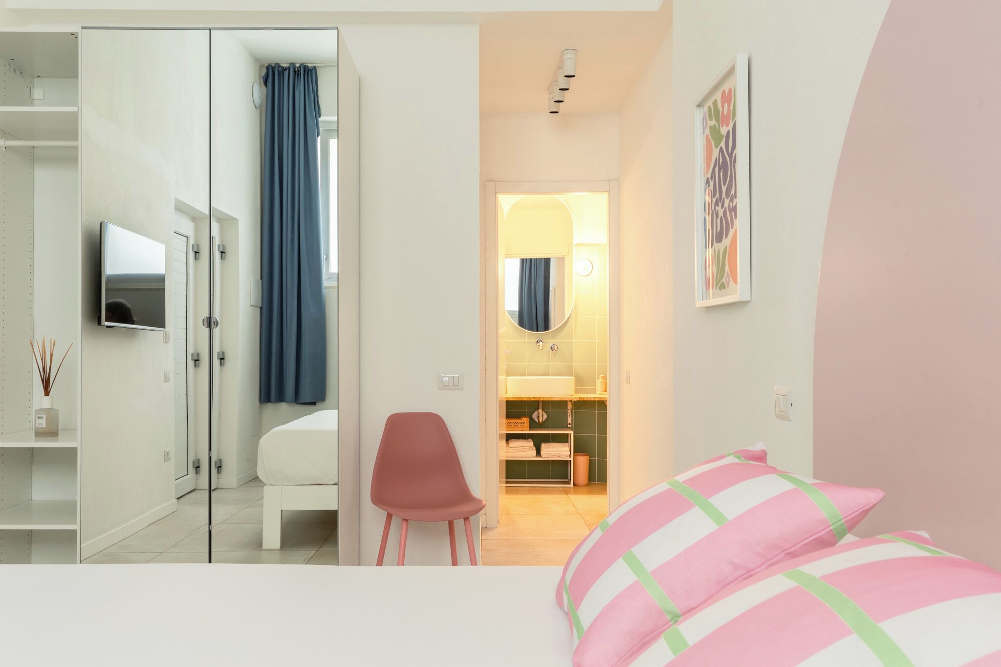 A modern bedroom with a bed, a chair, a TV, a bathroom with a mirror, and a shower.