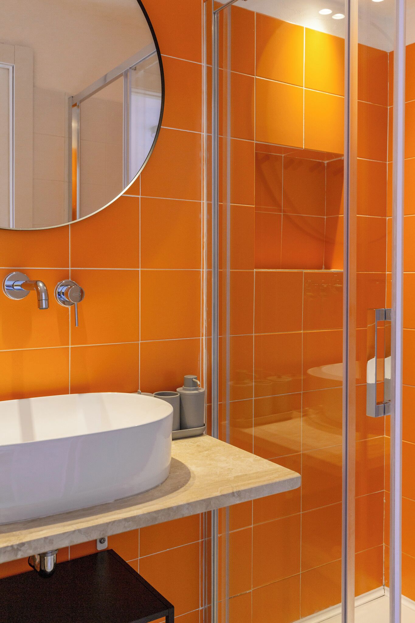 A bathroom with a white sink, a round mirror, and orange tiled walls.