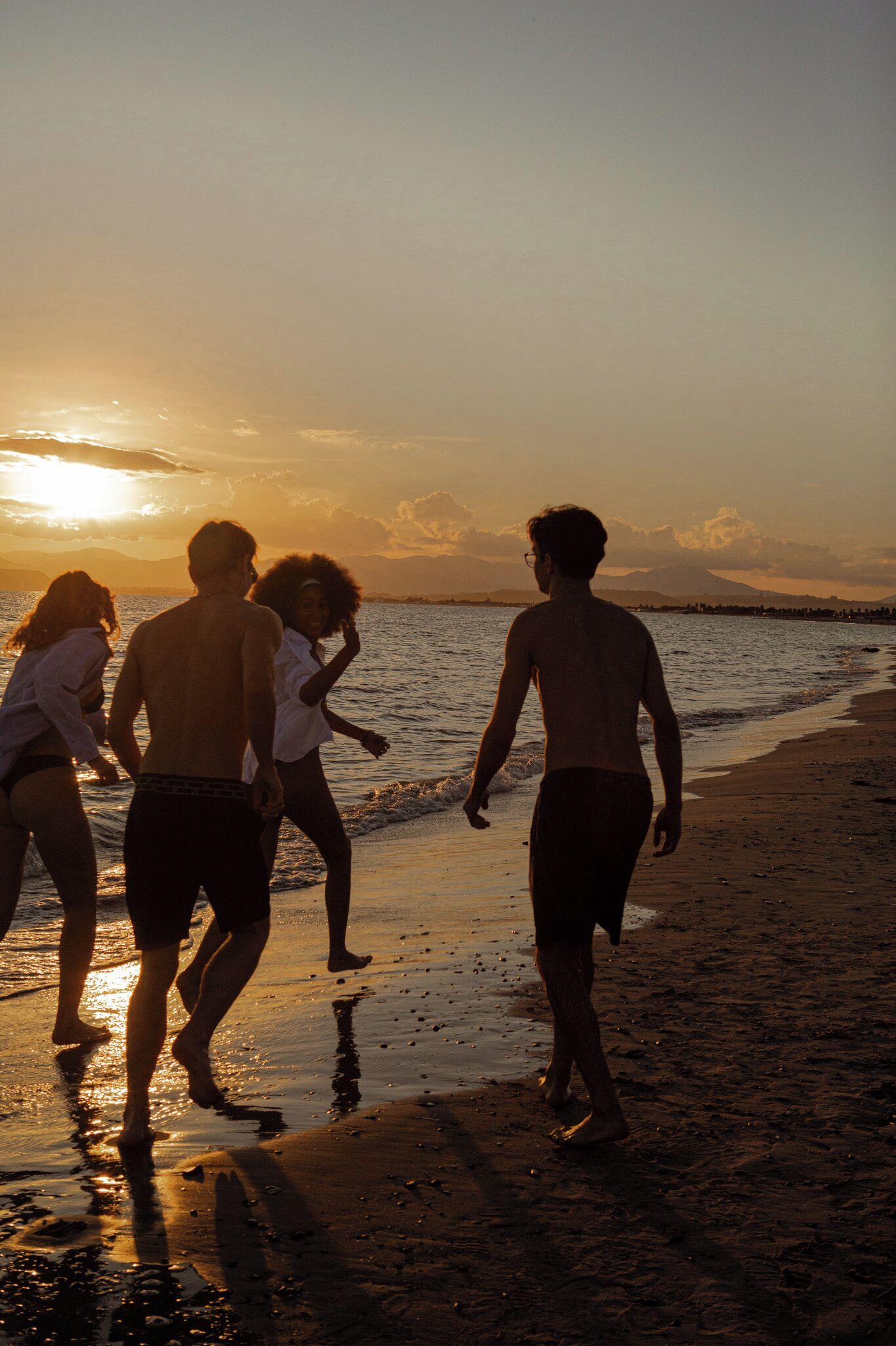 A group of people walking on a beach during sunset.