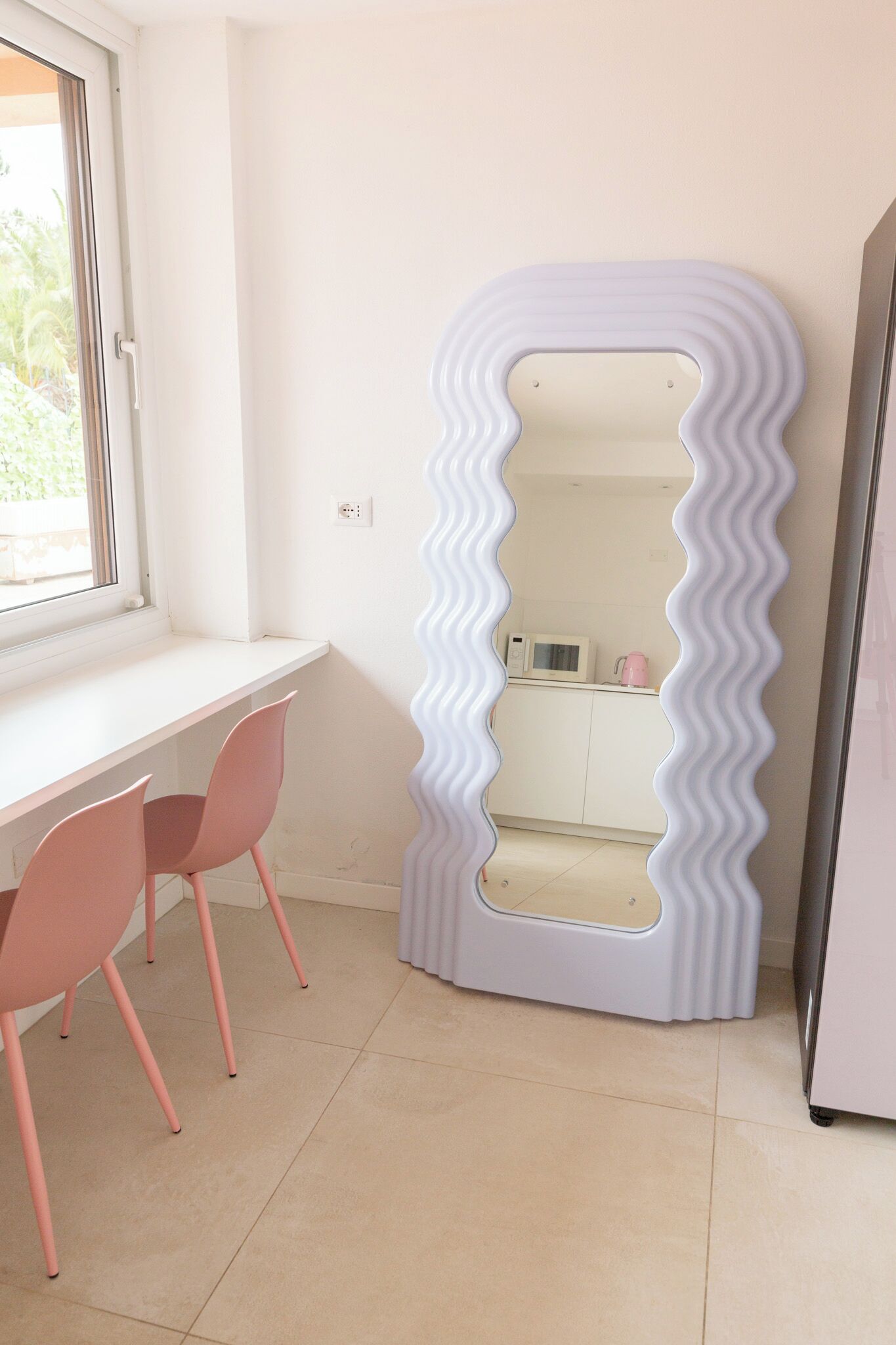 A room with a white desk, two pink chairs, a white microwave, and a white refrigerator.