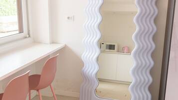 A room with a white desk, two pink chairs, a white microwave, and a white refrigerator.