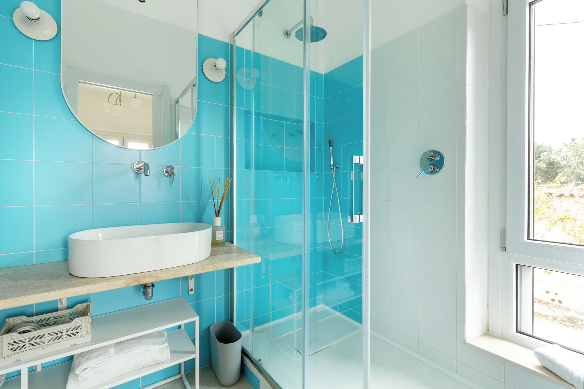 A modern bathroom with a large white sink, a glass shower enclosure, and a window providing natural light.