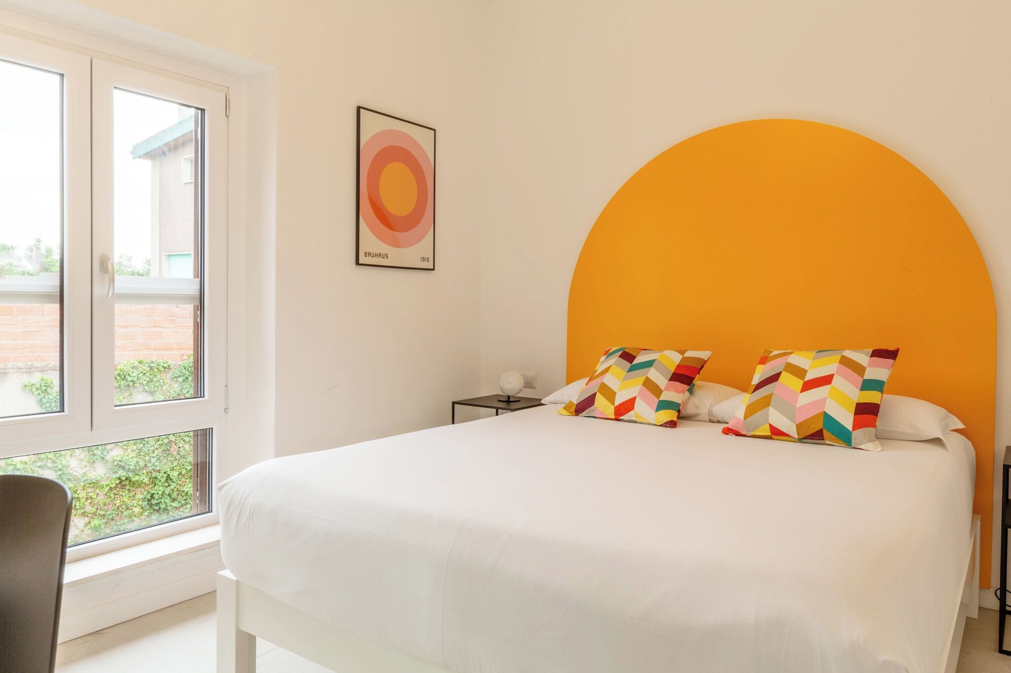 A bedroom with a large bed, a window, and a wall-mounted artwork.