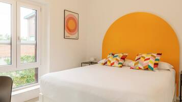 A bedroom with a large bed, a window, and a wall-mounted artwork.